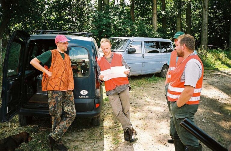 Vier Männer in Sicherheitswesten diskutieren bei Autos.