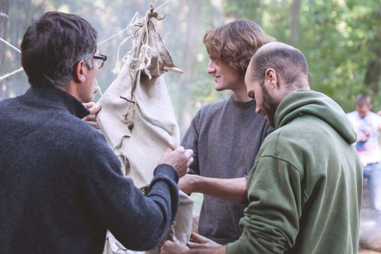 Drei Personen arbeiten an einer Stoffkonstruktion im Wald.