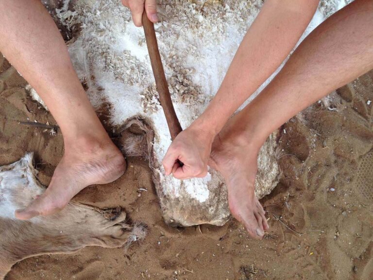 Traditionelle Lederverarbeitung mit Werkzeug auf Sandboden.