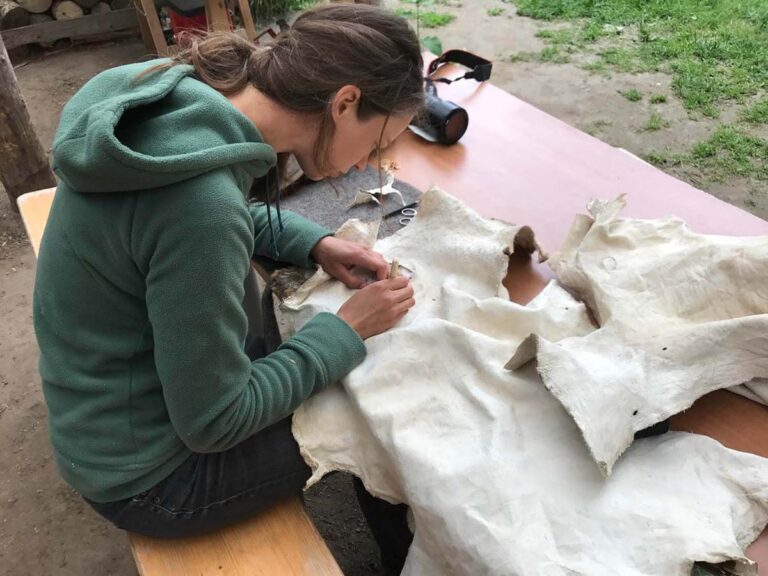 Person bearbeitet weiße Stoffe am Tisch draußen.