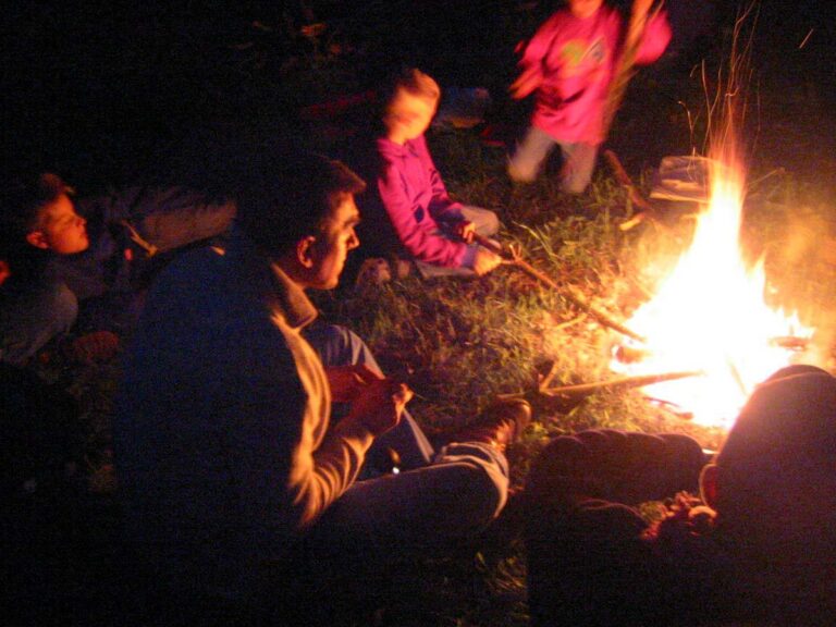 Menschen sitzen am Lagerfeuer im Freien.