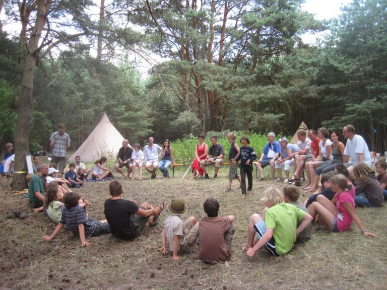 Menschen sitzen in einem Waldkreis mit Tipi.