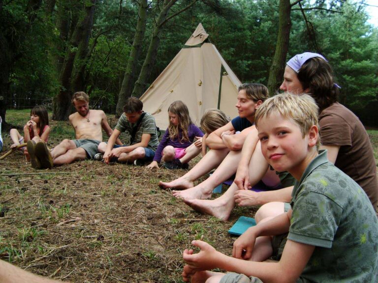 Gruppe sitzt im Wald vor einem Zelt.