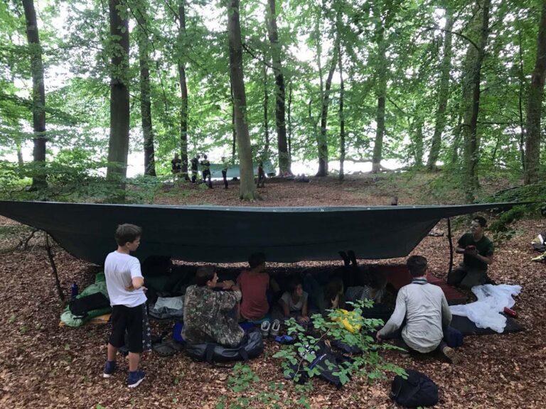 Kinder beim Campen im Wald unter einer Plane.