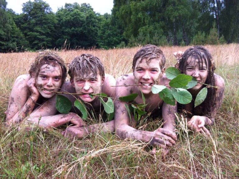 Vier lachende, schlammige Personen auf einer Wiese