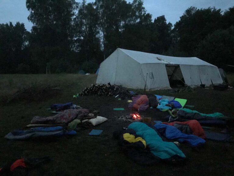 Campingplatz mit Zelten, Schlafsäcken und Feuer im Freien.