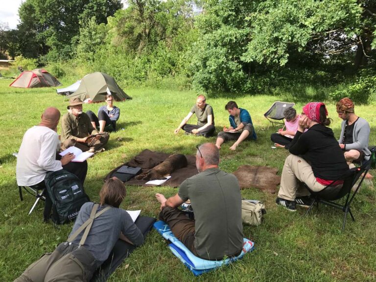 Gruppe im Kreis auf Wiese mit Zelten