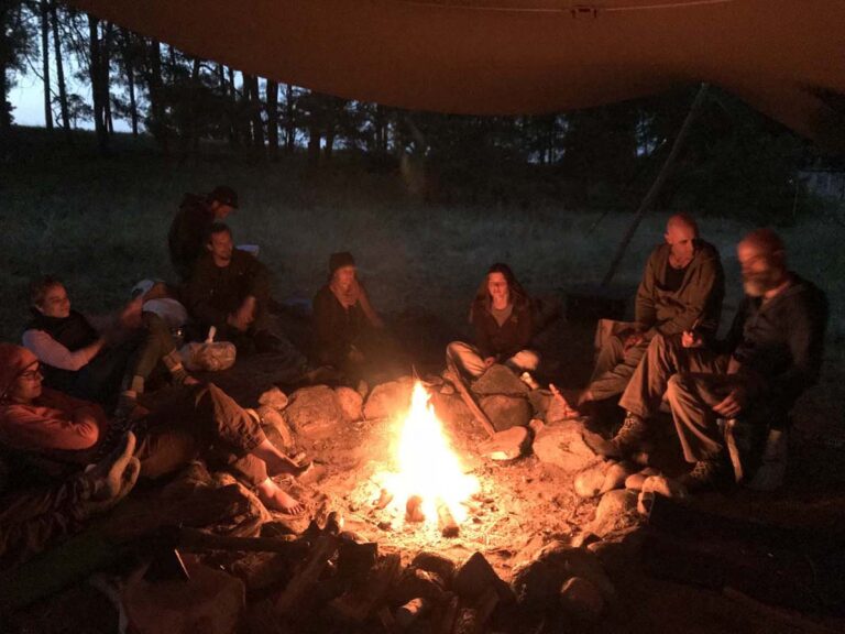 Menschen sitzen nachts um ein Lagerfeuer.
