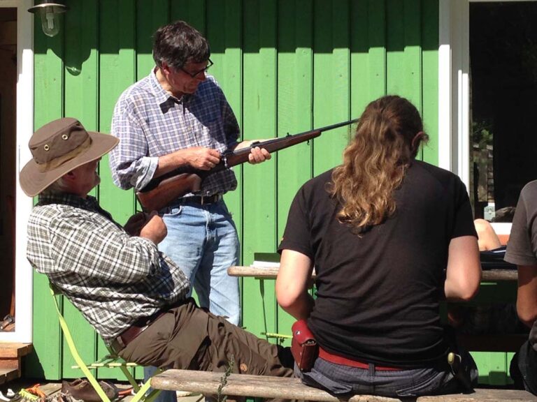 Männer mit Gewehr vor grünem Haus.