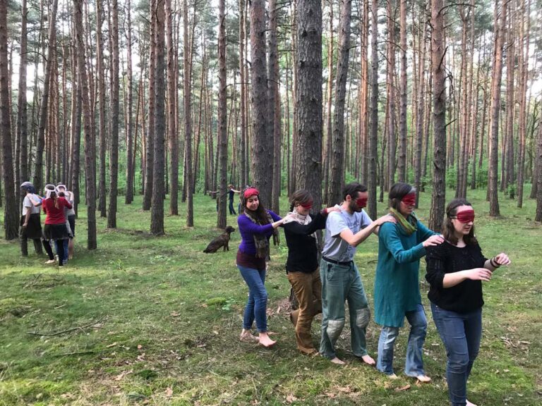 Menschen mit Augenbinden wandern durch den Wald.