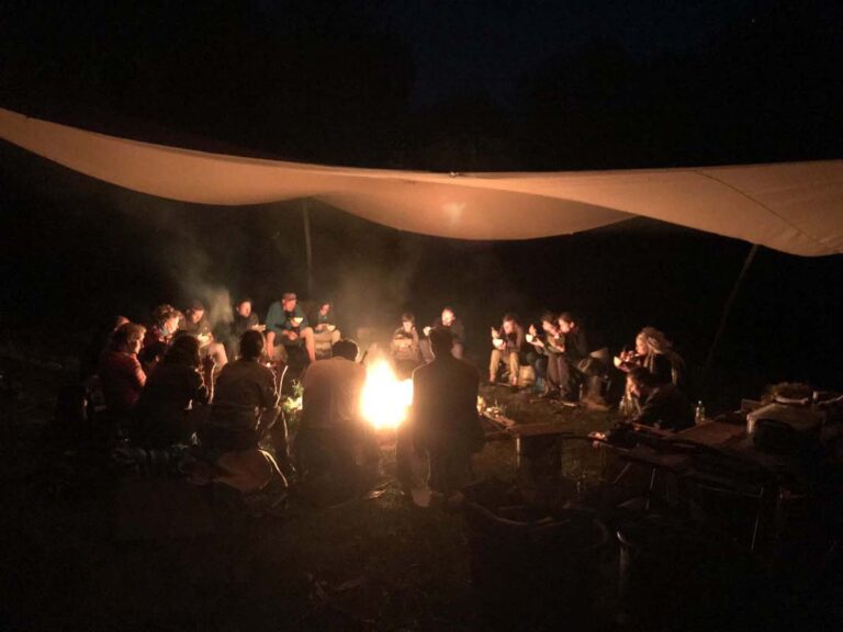 Menschen sitzen bei Nacht um ein Lagerfeuer.
