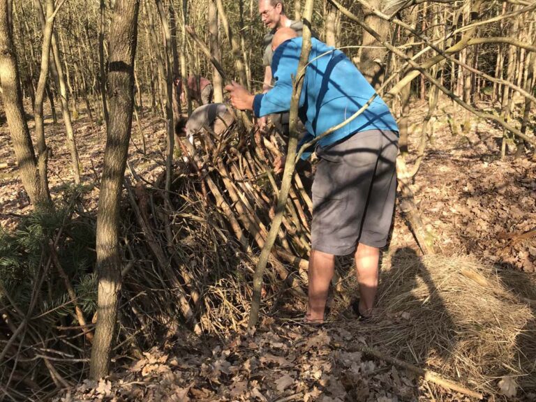 Mann baut Unterstand im Wald aus Ästen.