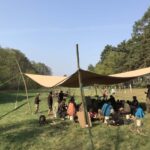 Gruppe Menschen unter Zeltdach im Freien.