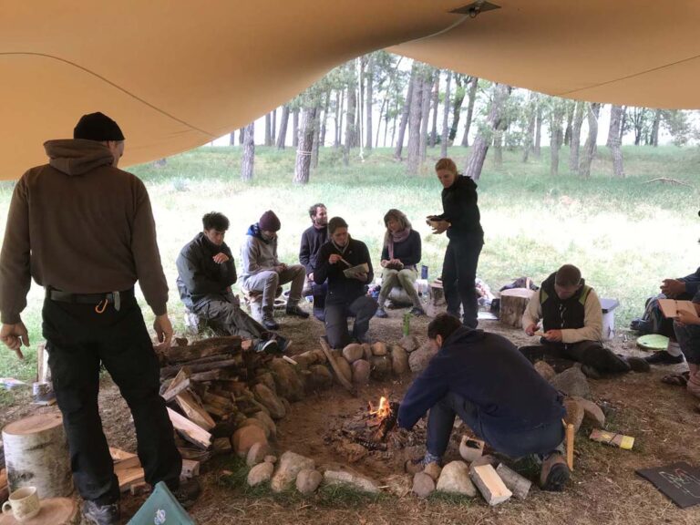 Gruppe um Lagerfeuer im Wald unter Zelt.
