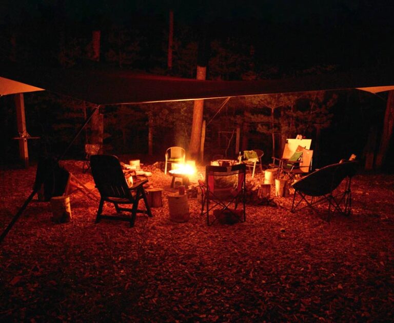 Nächtlicher Lagerfeuerplatz im Wald mit Stühlen.