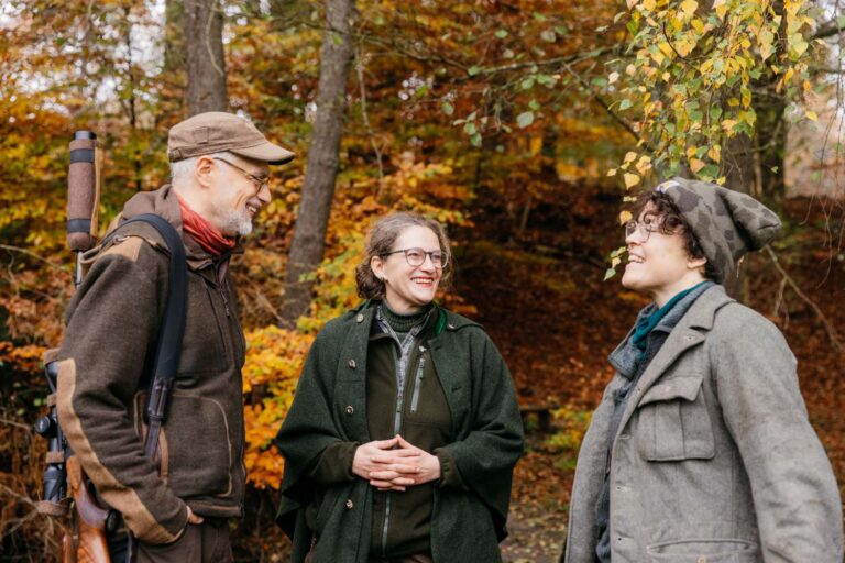 Drei Personen im Herbstwald unterhalten sich fröhlich.