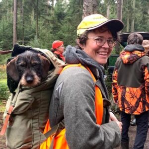 Frau mit Hund im Rucksack, Waldhintergrund.