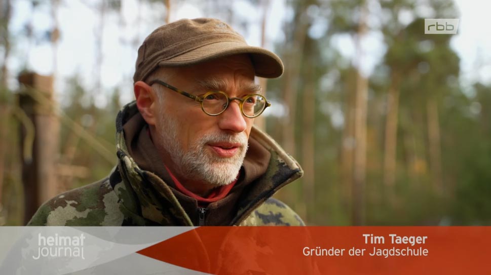 Person im Wald mit Camouflagejacke und Mütze.