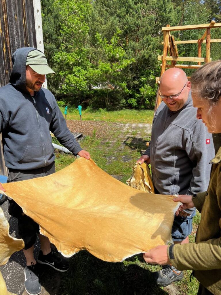 Drei Menschen, die ein gegerbtes Leder zwischen sich halten