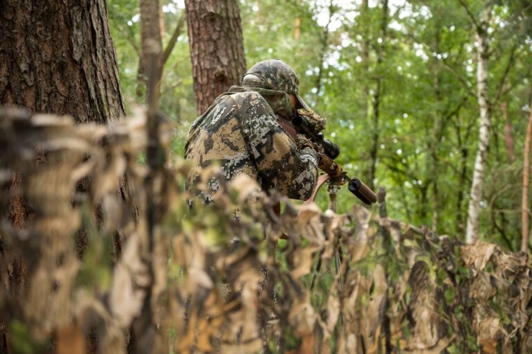 Getarnte Person im Wald mit Gewehr