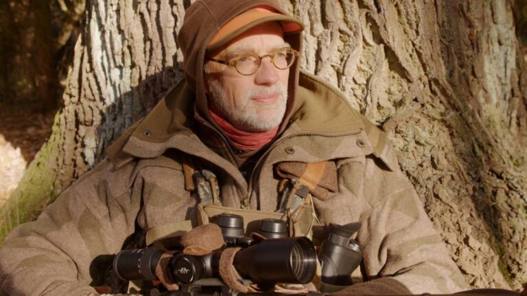 Mann mit Fernglas im Wald sitzend