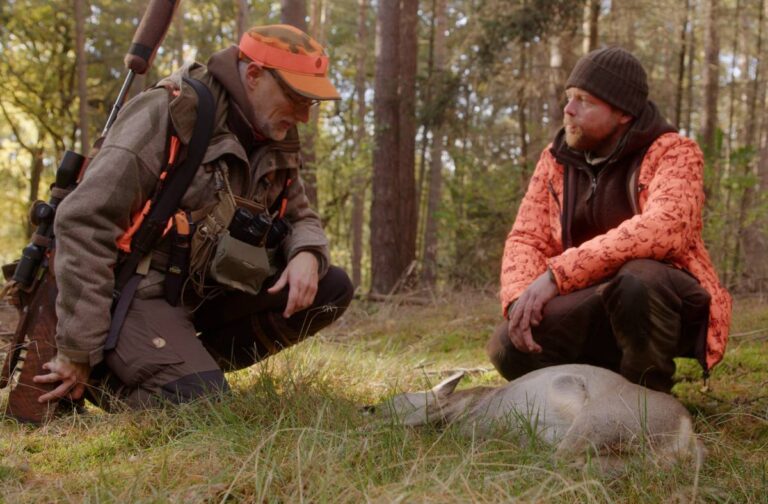 Zwei Jäger knien im Wald neben Wildtier.