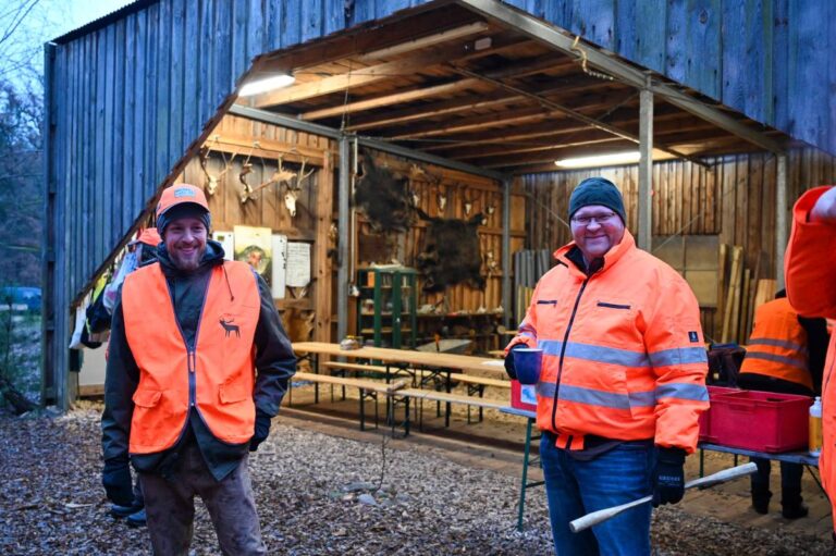 Jäger in orange Warnwesten vor Holzhütte