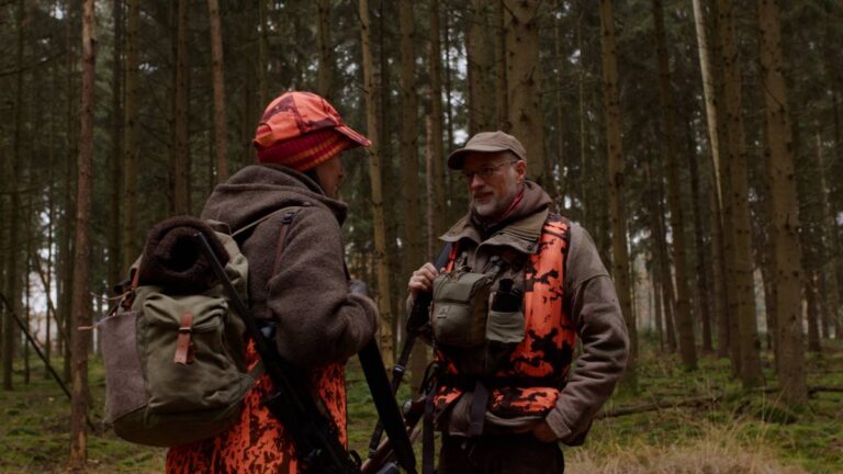 Zwei Personen im Wald, Jagdbekleidung tragend.
