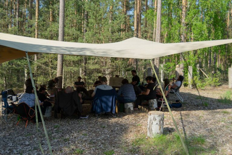 Gruppe sitzt unter Sonnensegel im Wald