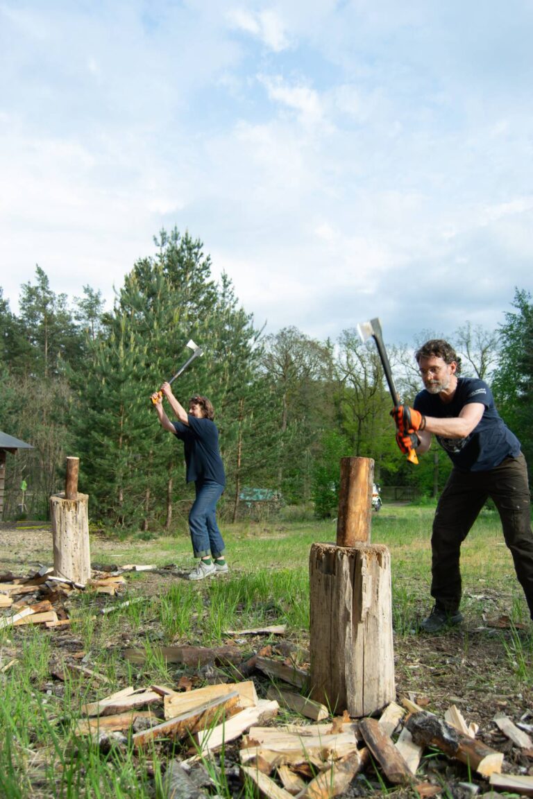 Zwei Personen hacken Holz im Freien.