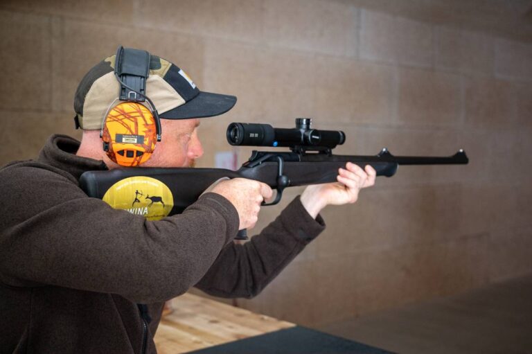 Mann zielt mit Gewehr unter Gehörschutz.